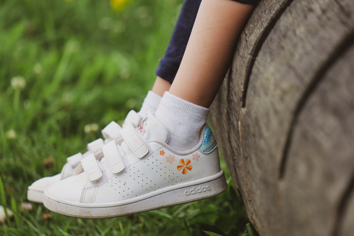Close-up of a child's feet with sneakers on a log in a grassy meadow, showcasing outdoor play.