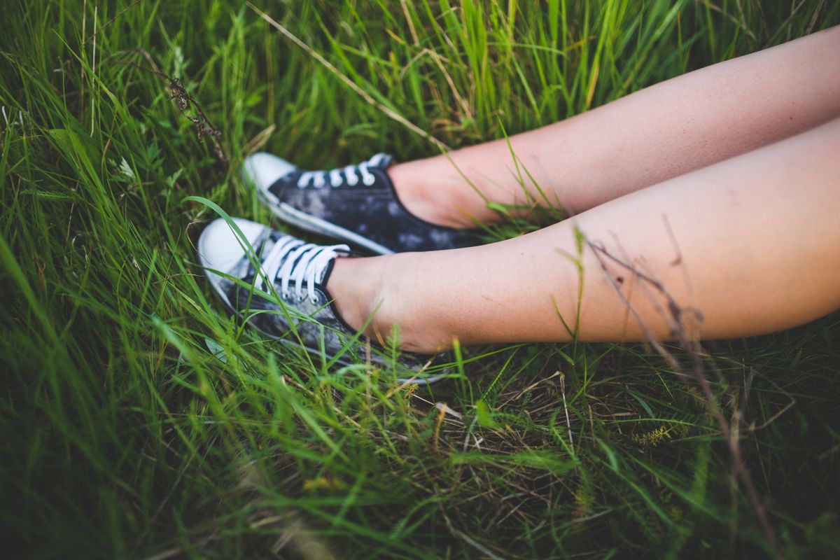 Person lying in green grass wearing sneakers, enjoying nature's calm.