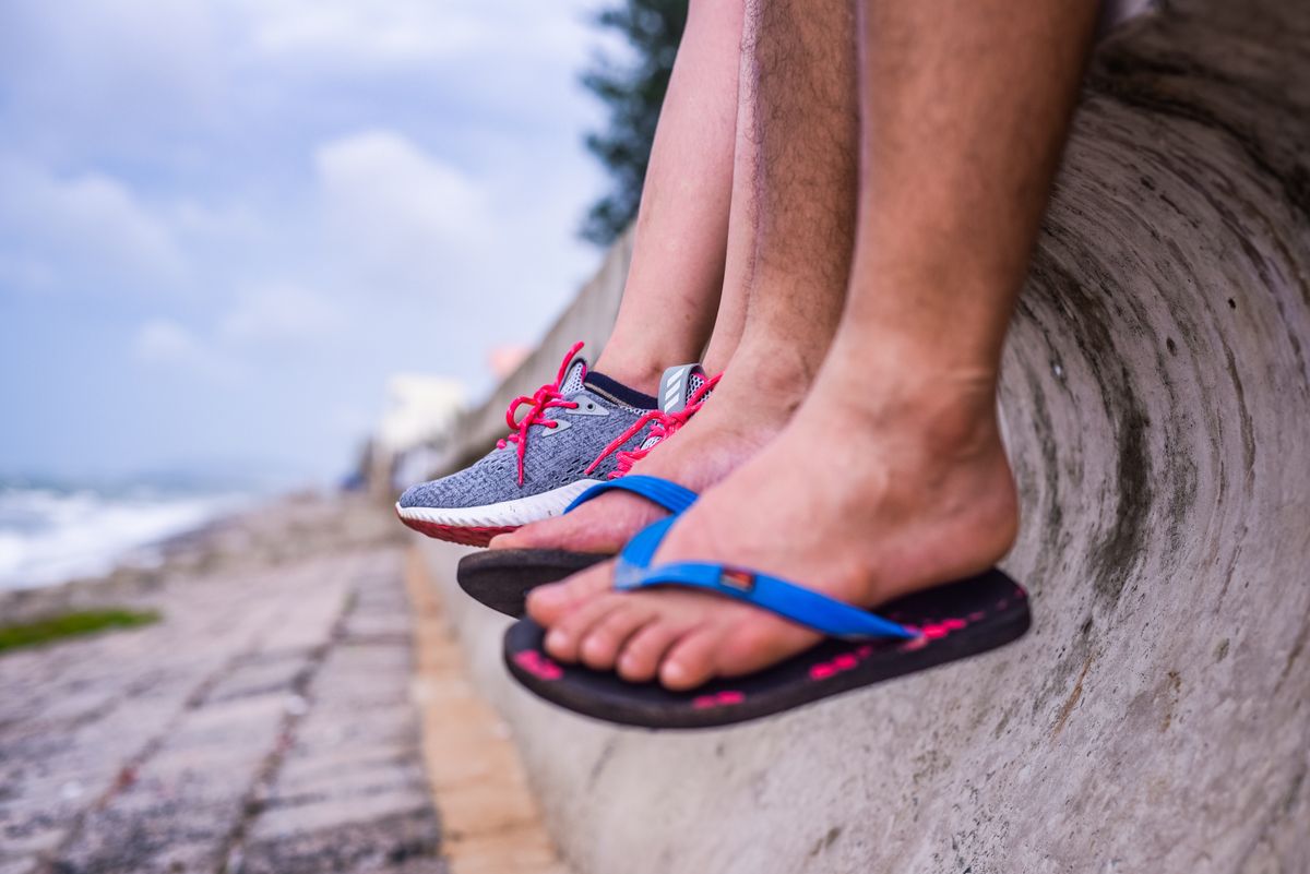 Feet in sneakers and flip-flops resting on a seaside wall with ocean view.