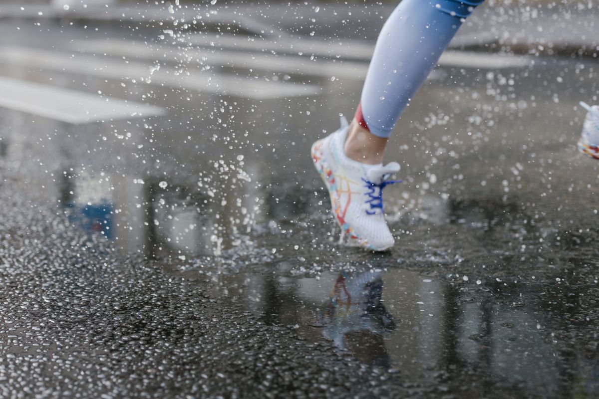 Close-up of runner's feet in sneakers splashing through puddles on a wet street.