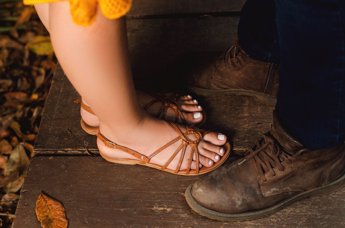Close-up of feet in sandals and boots on a wooden deck with autumn leaves.