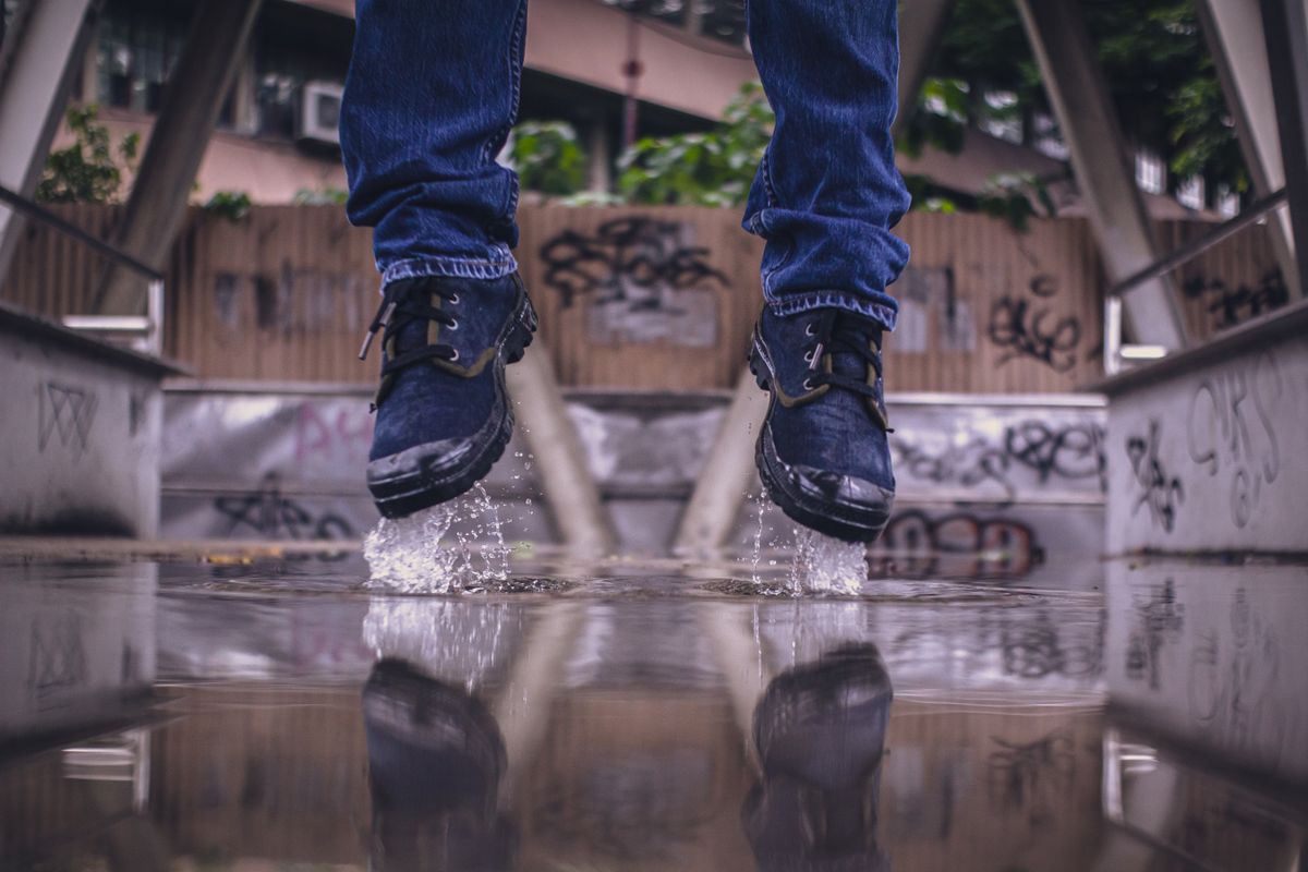 Close-up of boot-clad feet splashing in a puddle with urban graffiti background.