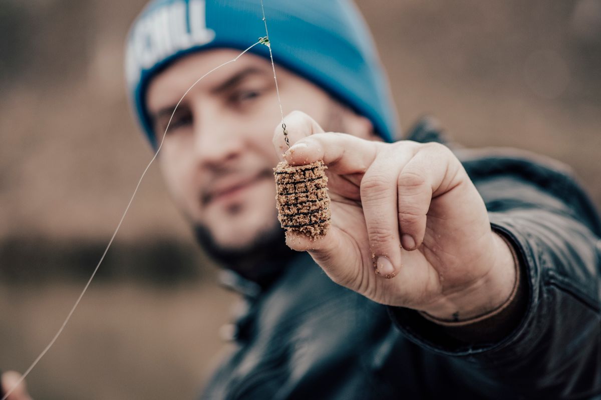 A fisherman holding a fishing lure, showcasing detailed bait and blurred background.