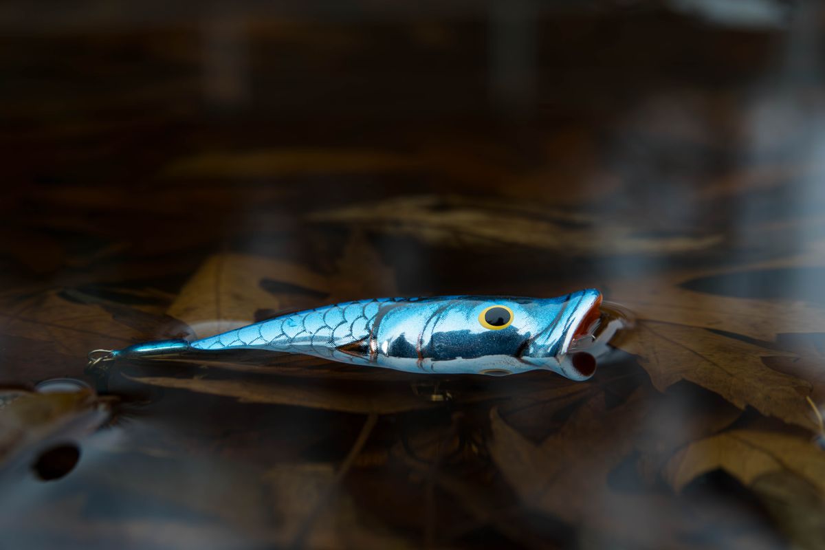 A detailed shot of a colorful blue fishing lure floating on water with leaves.