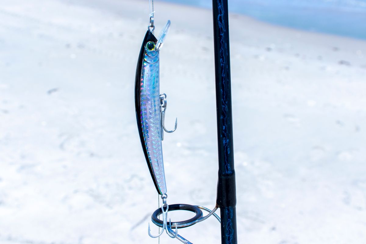 Detailed view of a fishing lure attached to a rod on a sandy beach, ideal for fishing lovers.