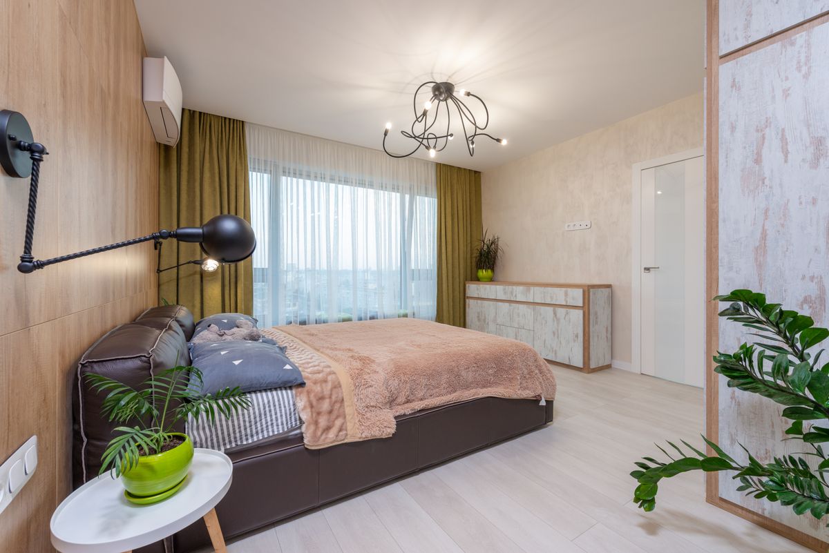 Interior of contemporary bedroom with large comfortable bed and green potted plants in flat in daytime