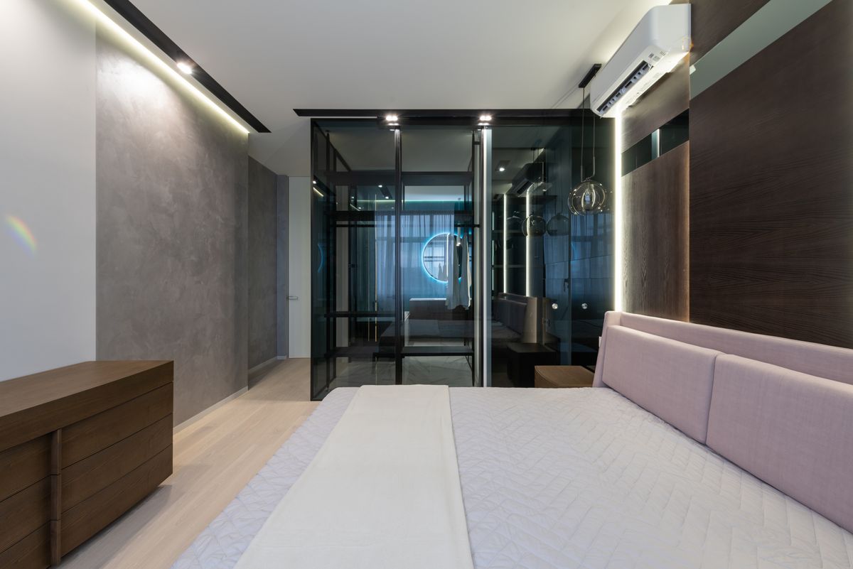 Interior of cozy bedroom with comfy bed and bathroom with glass walls in modern apartment