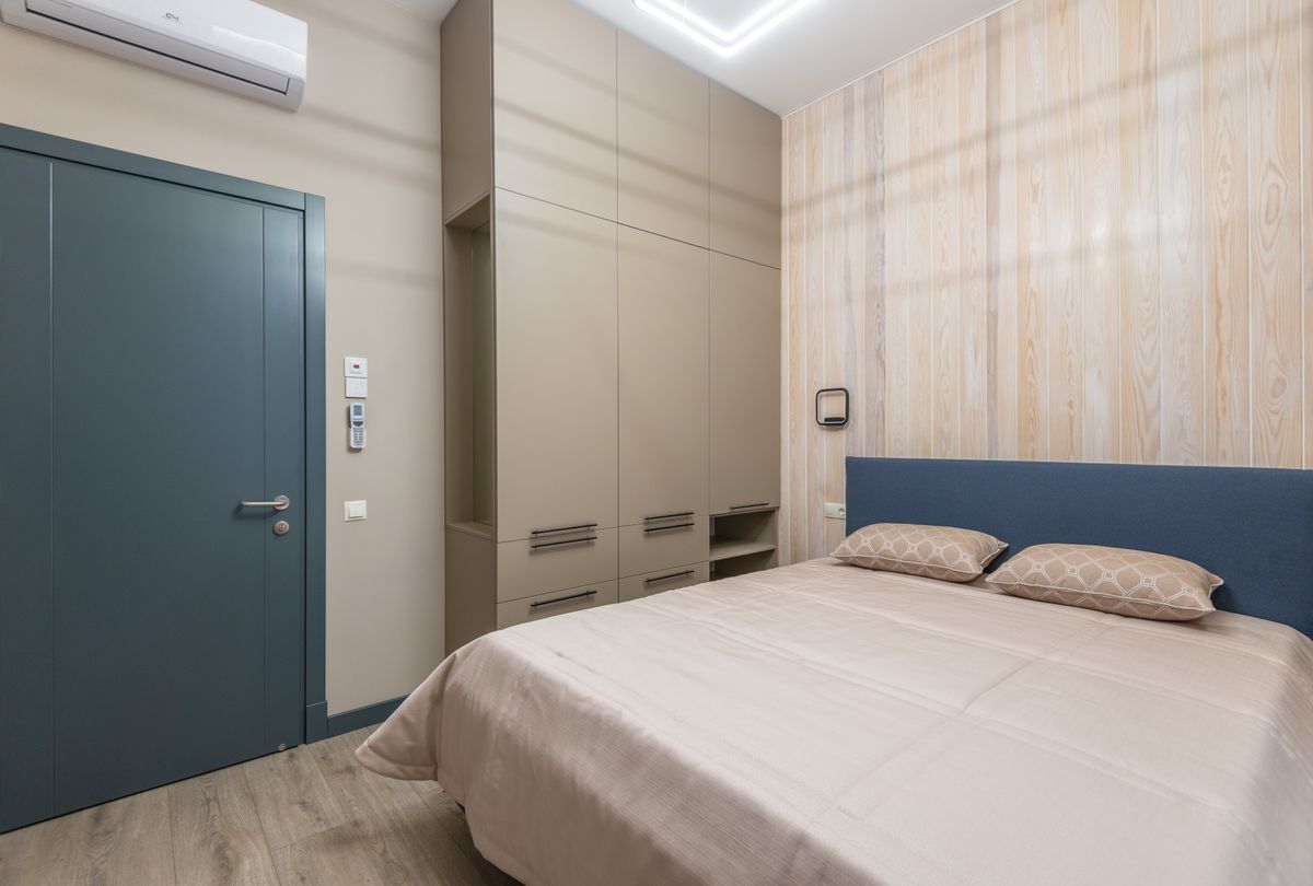 Interior of cozy bedroom with comfortable bed with pillows and coverlet and wardrobe near door