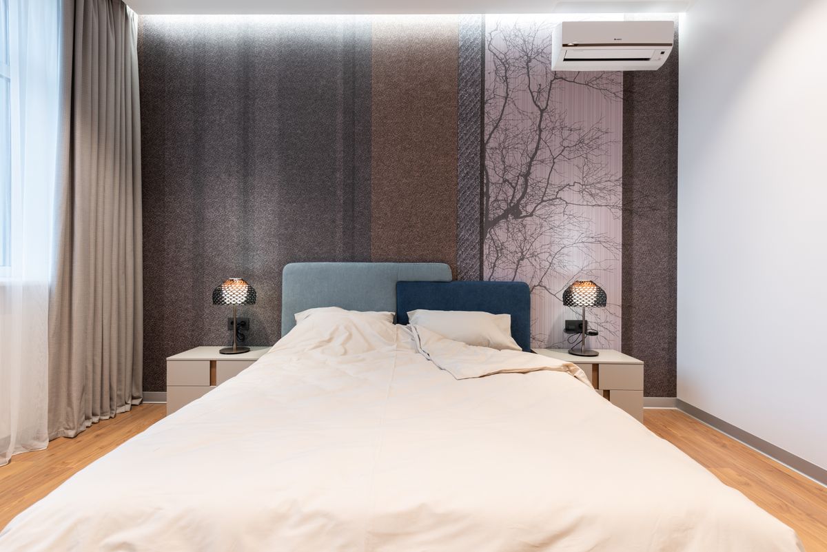 Interior of modern bright room with bed near table with lamp near wall and window with curtains and wooden floor