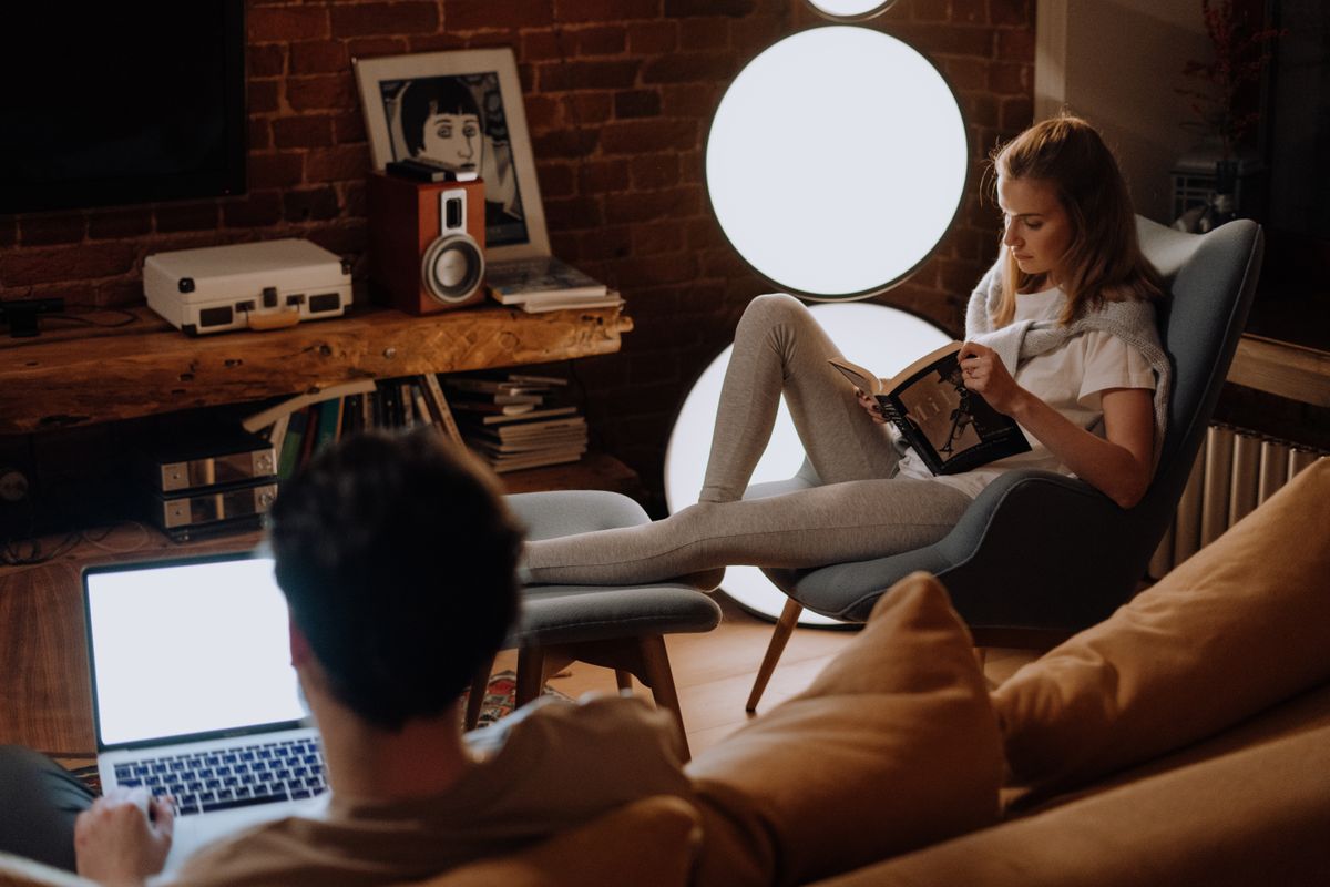 Couple relaxing at home, with laptop and book, in a cozy living room.