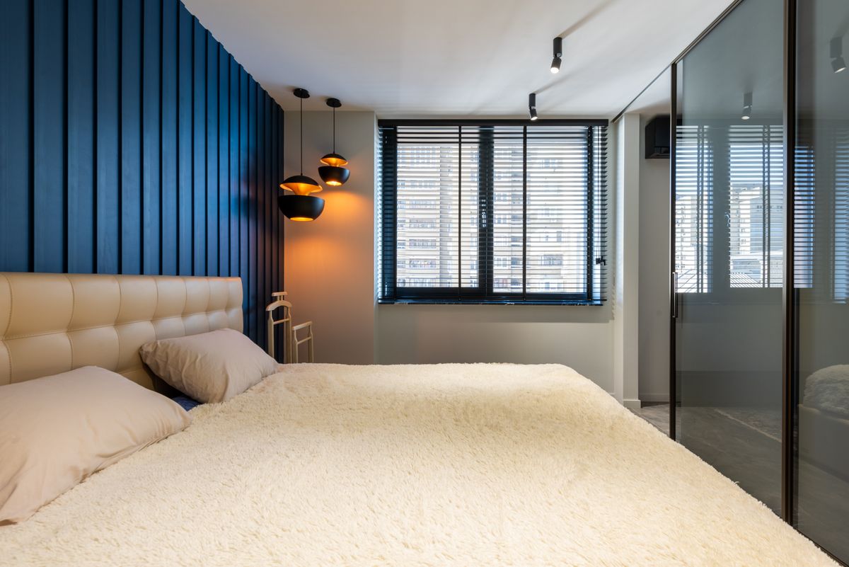 Contemporary bedroom interior with coverlet and pillows on bed against lamps and glass wall in light apartment