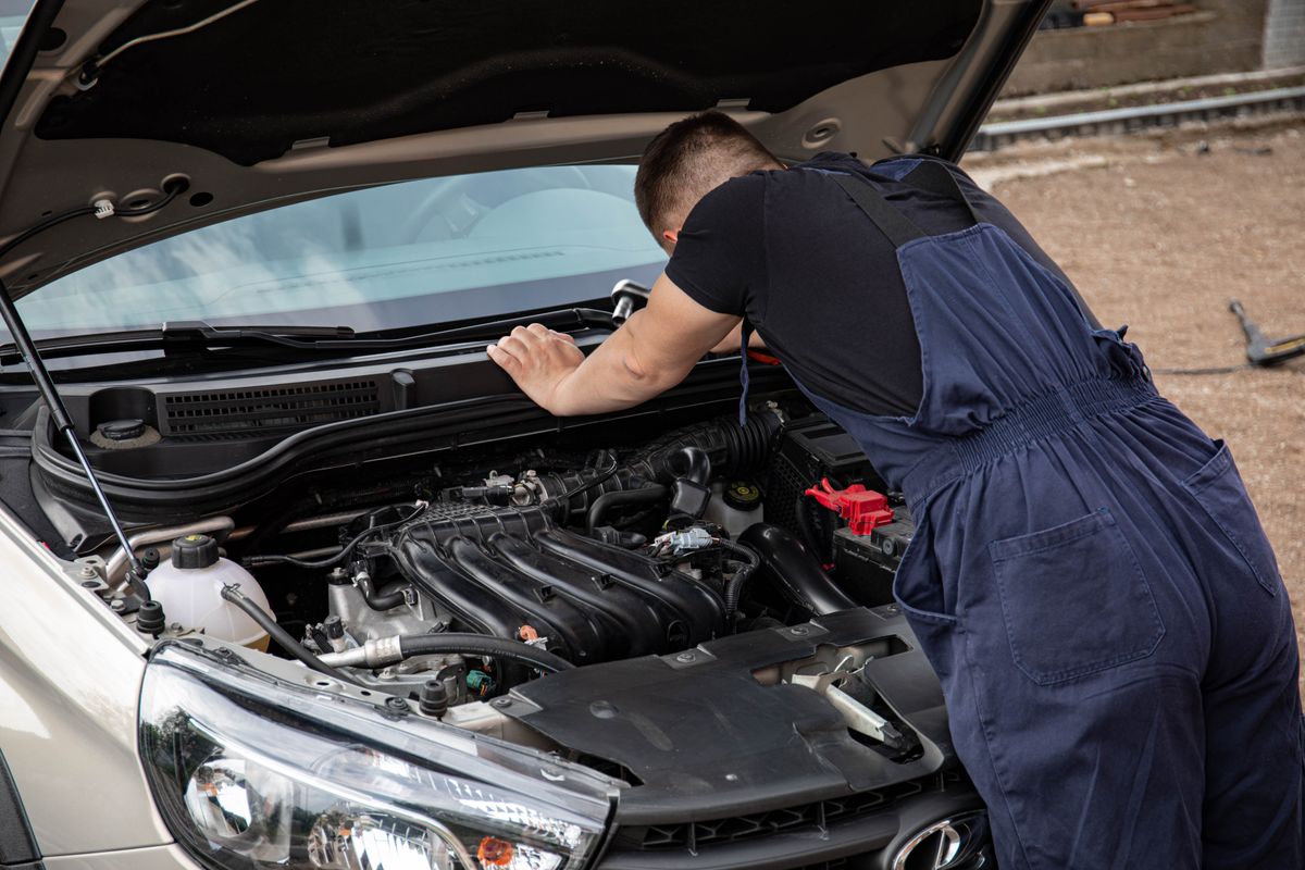 Mechanic checking car engine outdoors, focusing on vehicle maintenance and repair.