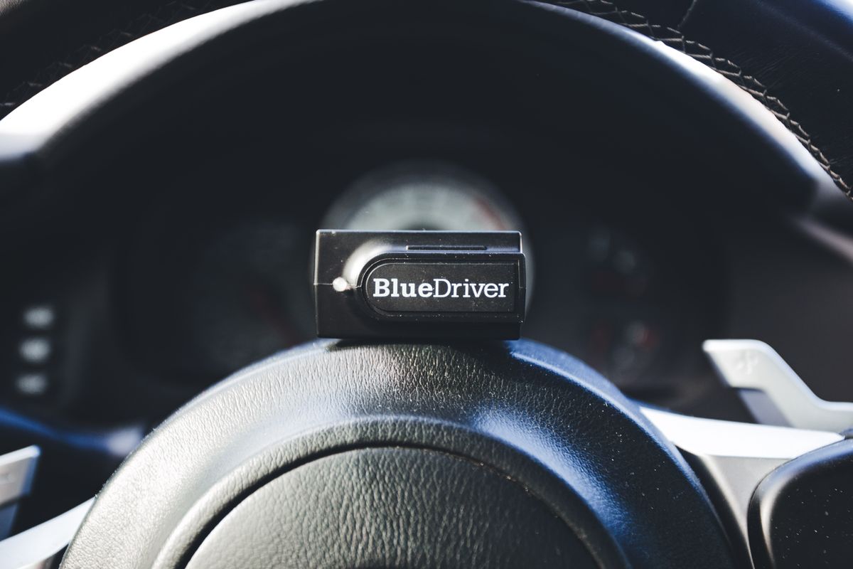 A BlueDriver code reader placed on a car's steering wheel, showcasing automotive diagnostic tools.