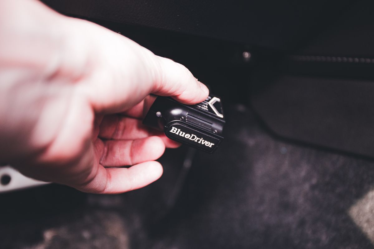 Close-up of a hand connecting a BlueDriver diagnostic device in a vehicle. Ideal for automotive and technology themes.