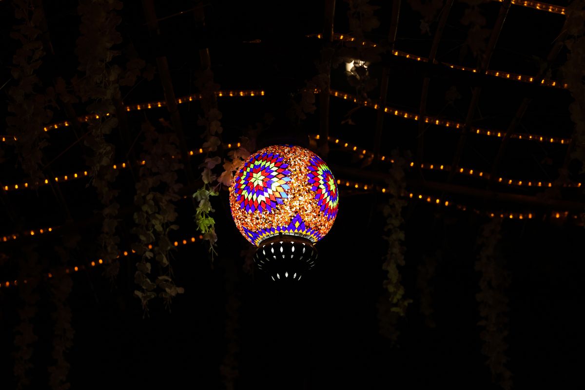 Vibrant mosaic lantern suspended in the dark, surrounded by string lights.