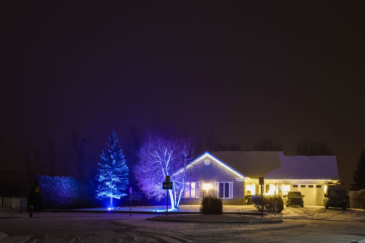 A cozy home exterior beautifully decorated with lights during a snowy winter night.