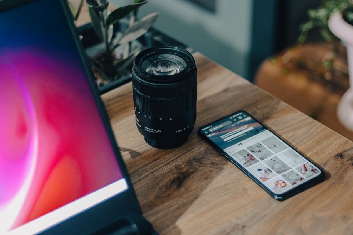A camera lens beside a smartphone on a wooden desk, showcasing modern technology.
