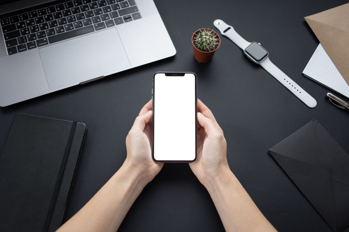 Hands holding a smartphone with blank screen on a minimalist office desk setup.
