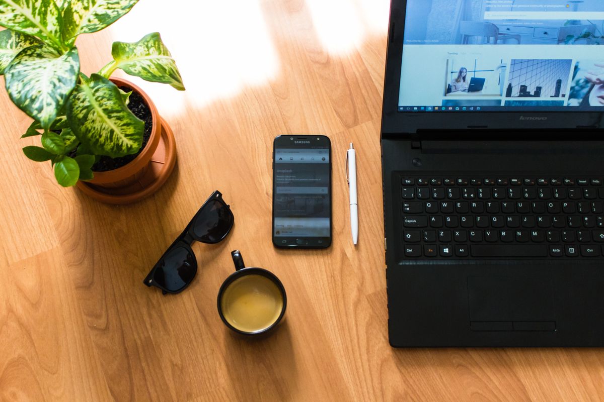 Stylish workspace featuring a laptop, smartphone, coffee, and a plant on a wooden desk.
