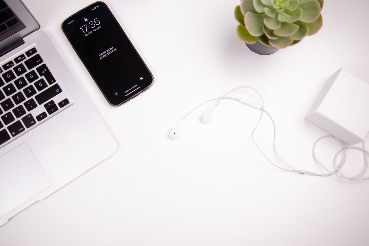 Elegant minimalist workspace featuring a laptop, smartphone, earbuds, and succulent on a white desk.