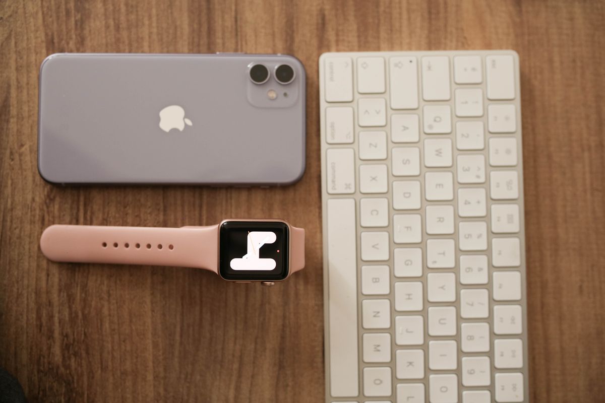 Flat lay of smartphone, smartwatch, and keyboard on a wooden desk, showcasing modern tech accessories.