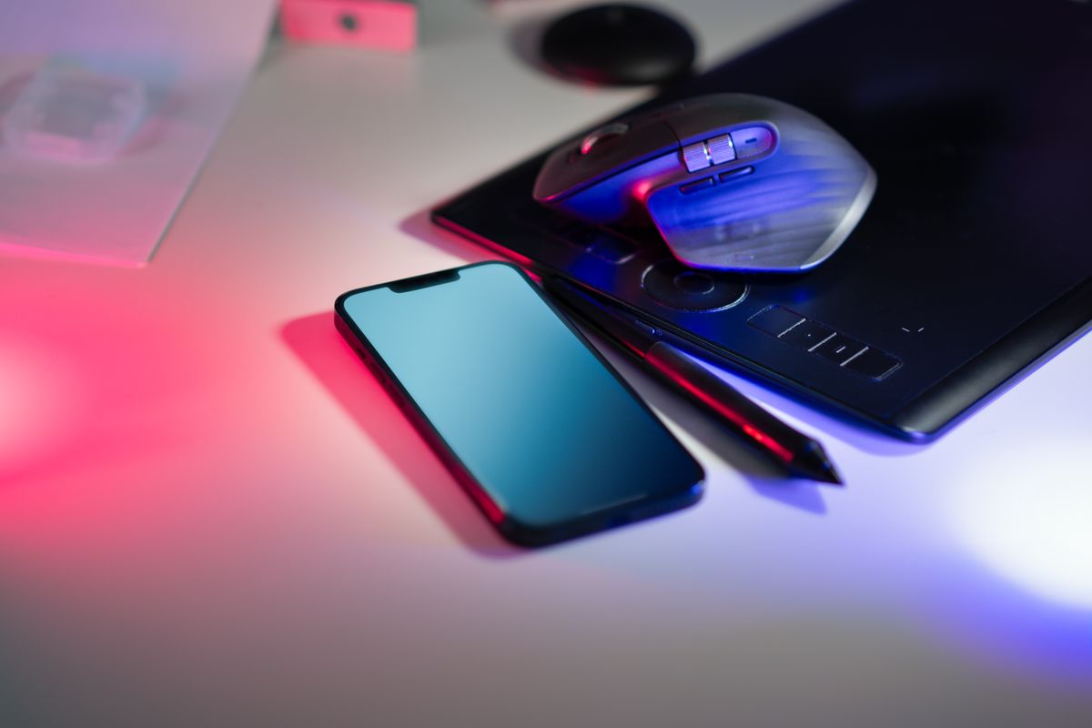 Modern workspace featuring a stylus tablet, smartphone, and computer mouse under colorful lighting.
