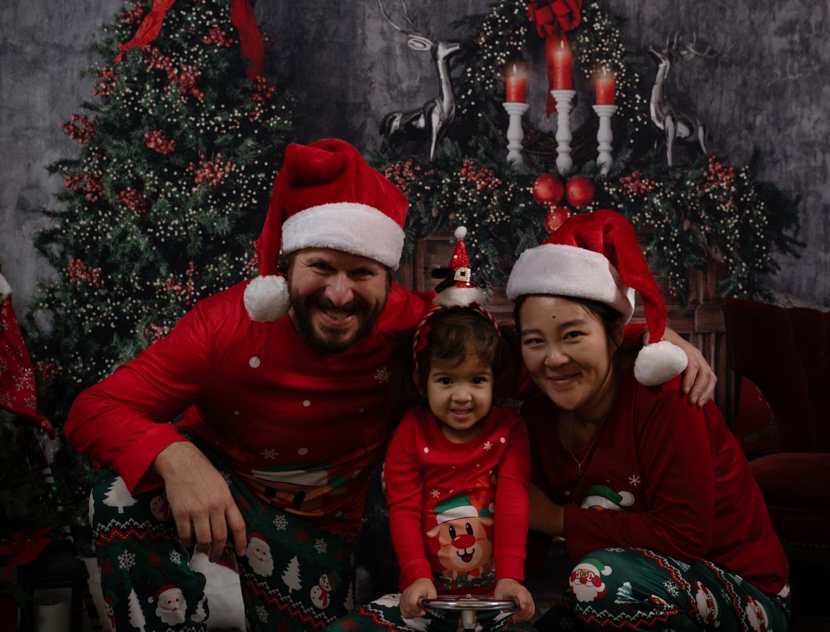 Family wearing Santa hats and Christmas pajamas, smiling by decorated tree, Chicago.