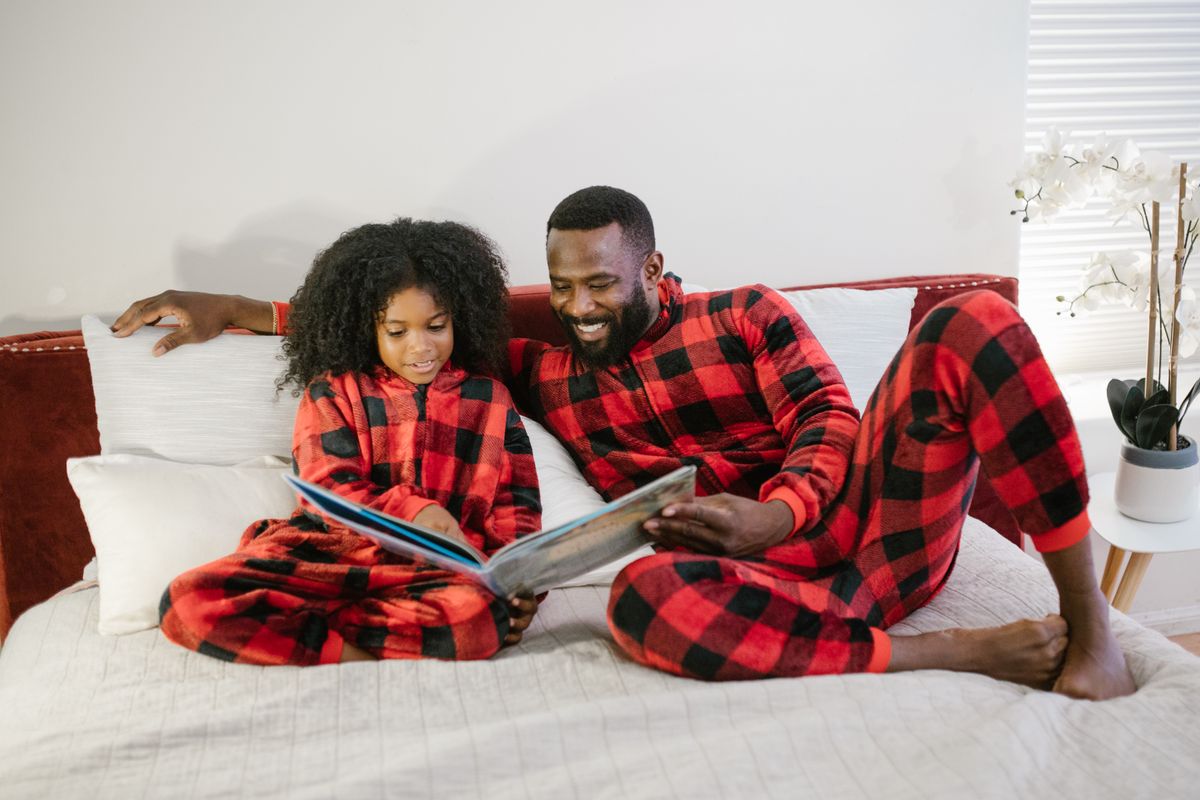 A father and daughter enjoy reading together in matching red plaid pajamas, fostering family bonding at bedtime.
