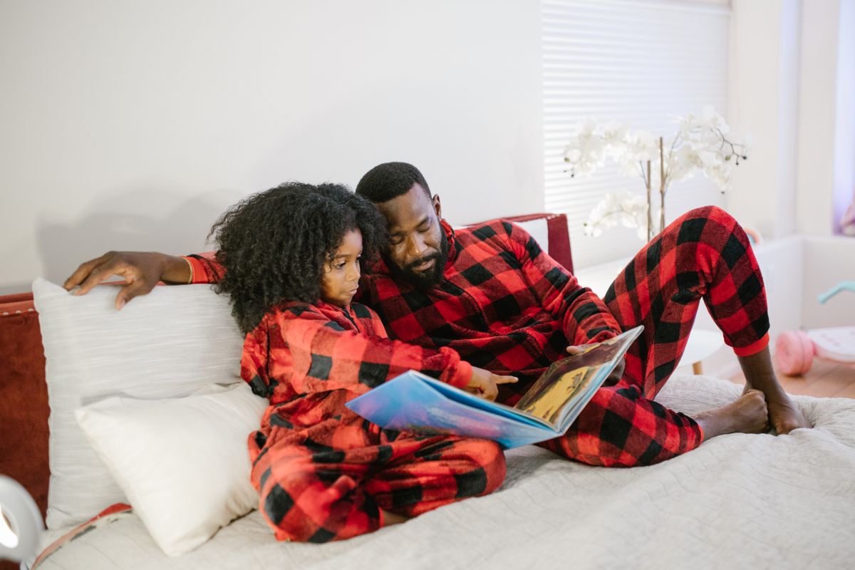 Father and daughter in matching pajamas reading a book together on a bed, creating a warm family moment.