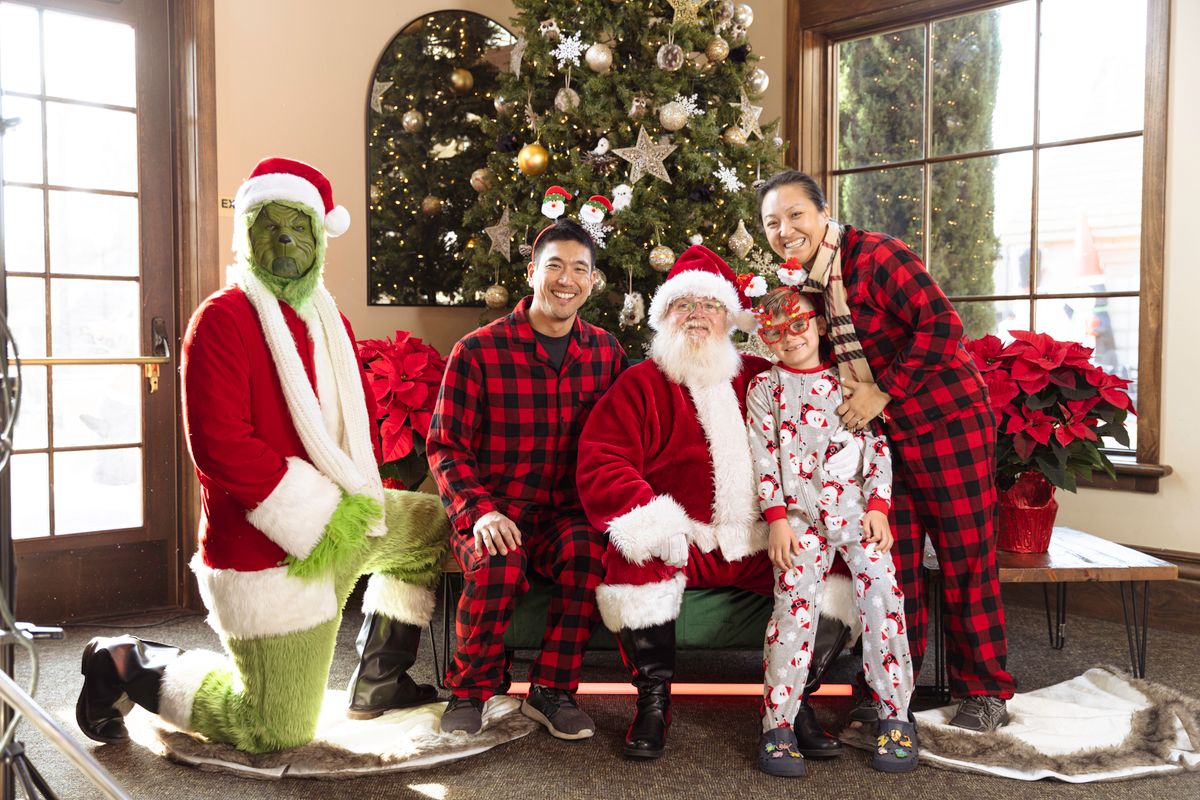 Festive family photo with Santa Claus, the Grinch, and Christmas tree indoors.