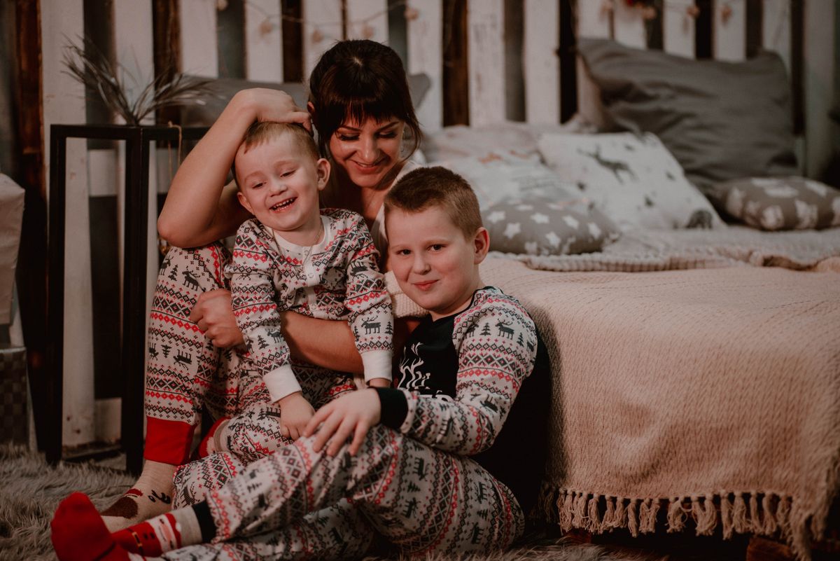 Mother and sons in matching Christmas pajamas sharing a joyful moment indoors.