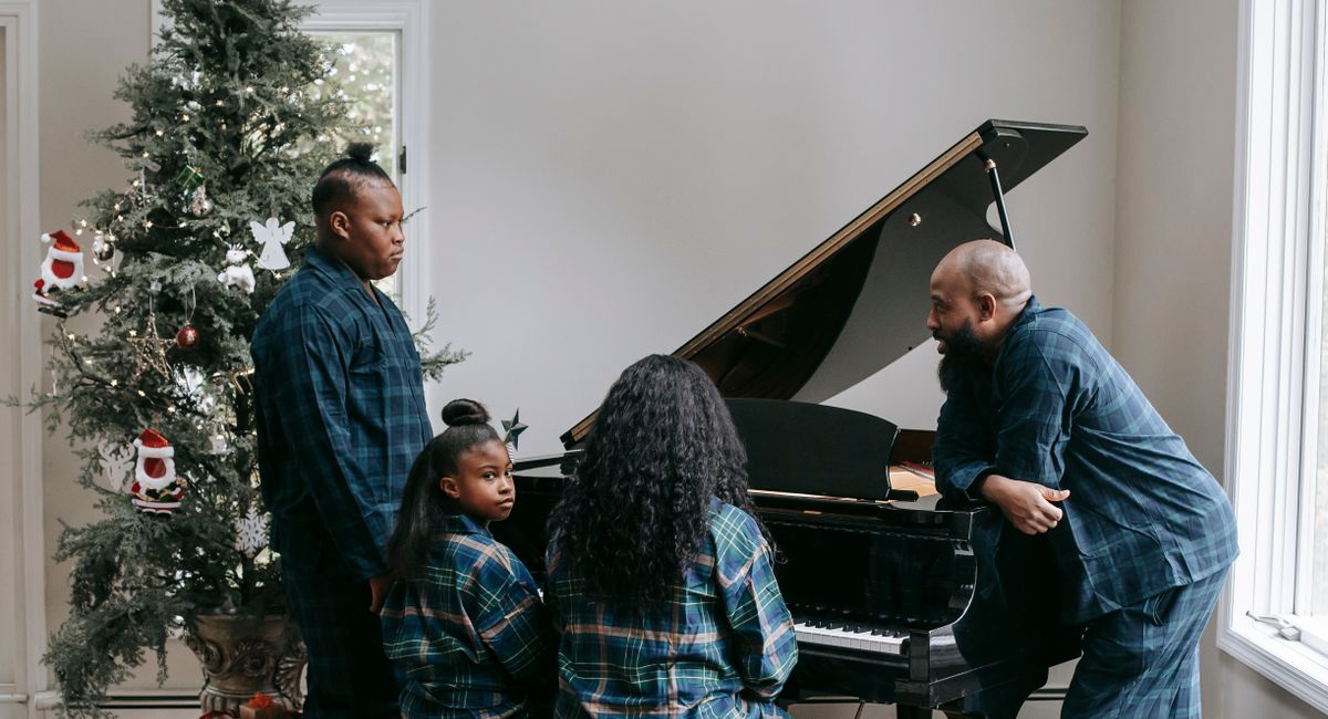 African American family playing musical instrument together in room decorated with shining Christmas tree