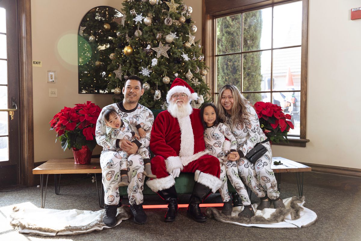 Family in matching pajamas posing with Santa Claus by Christmas tree indoors.