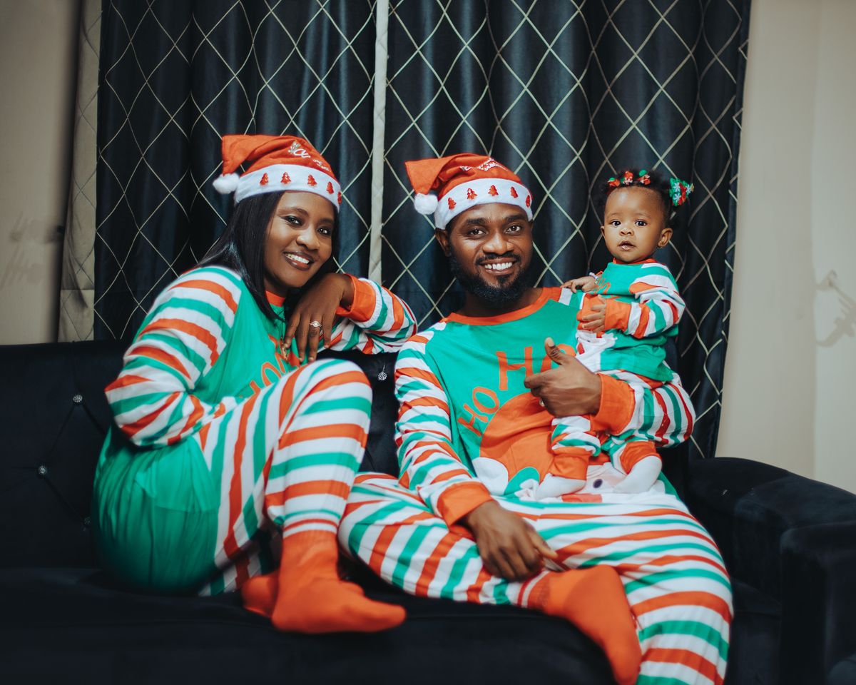 Happy family celebrating Christmas in matching pajamas with Santa hats, indoors on a cozy sofa.