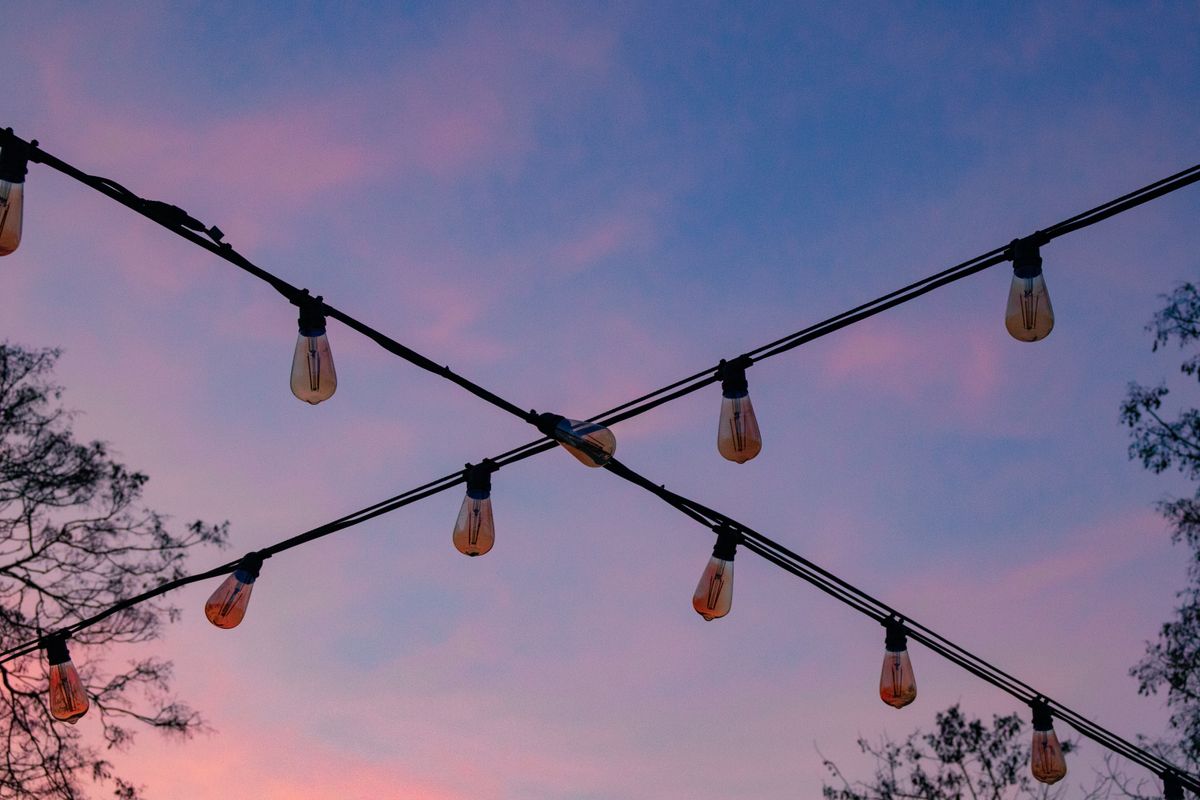 Outdoor string lights hanging with a colorful dusk sky in the background.
