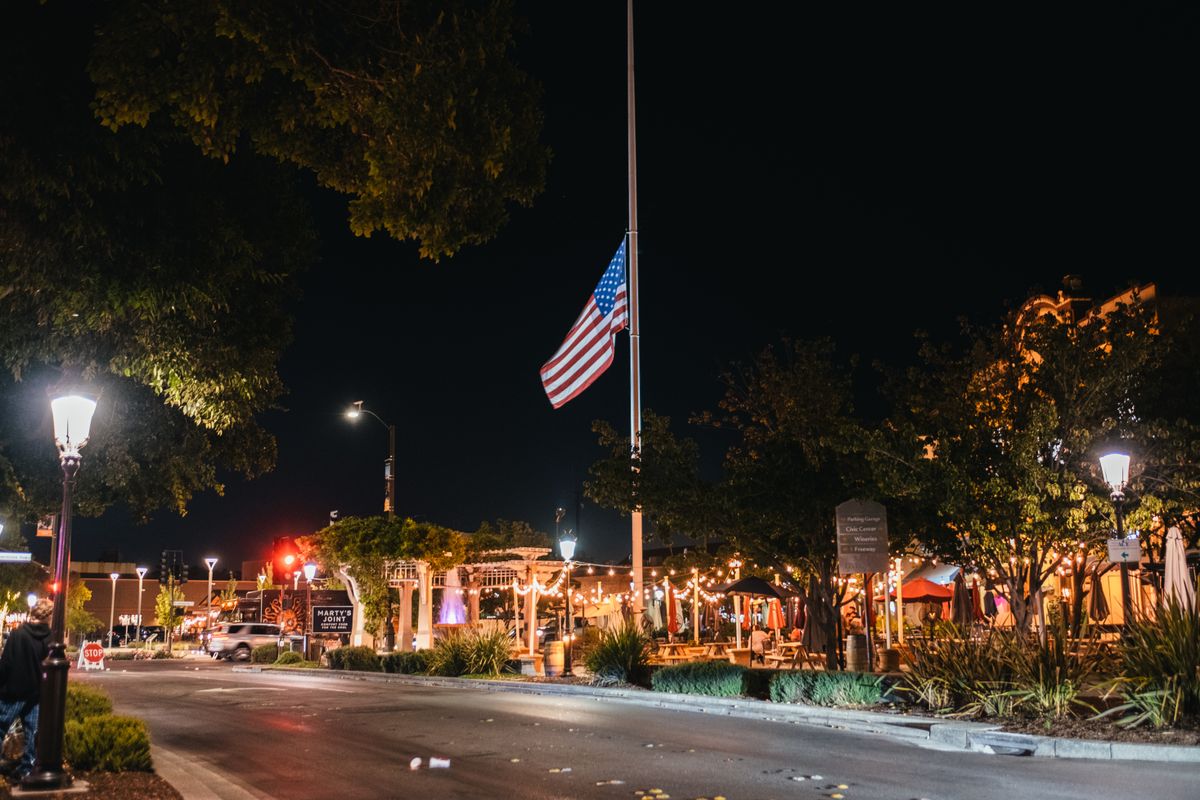 A lively street scene at night with an American flag and bright lights, showcasing city life.