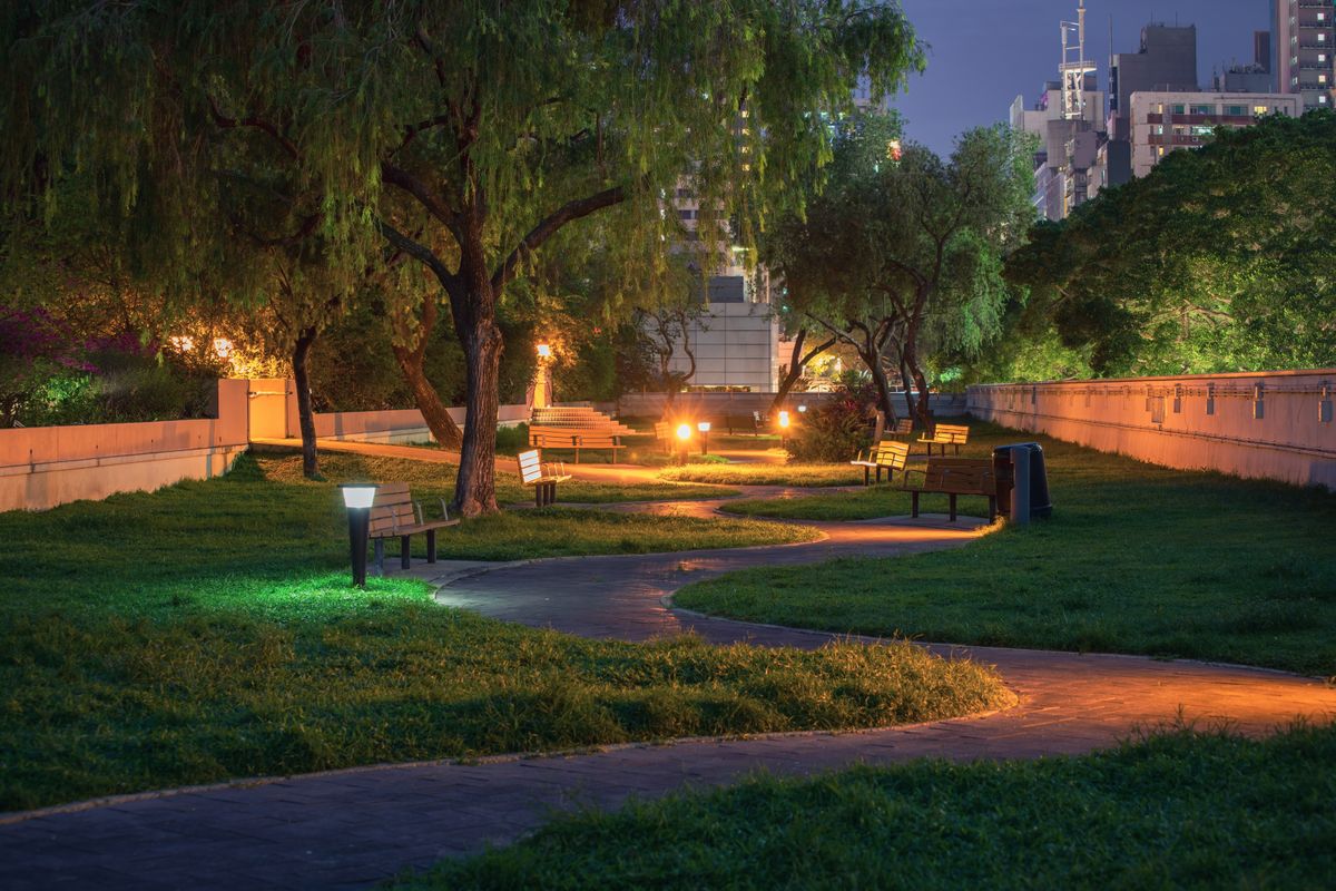 Peaceful urban park at night featuring a winding path and lamp-lit benches.