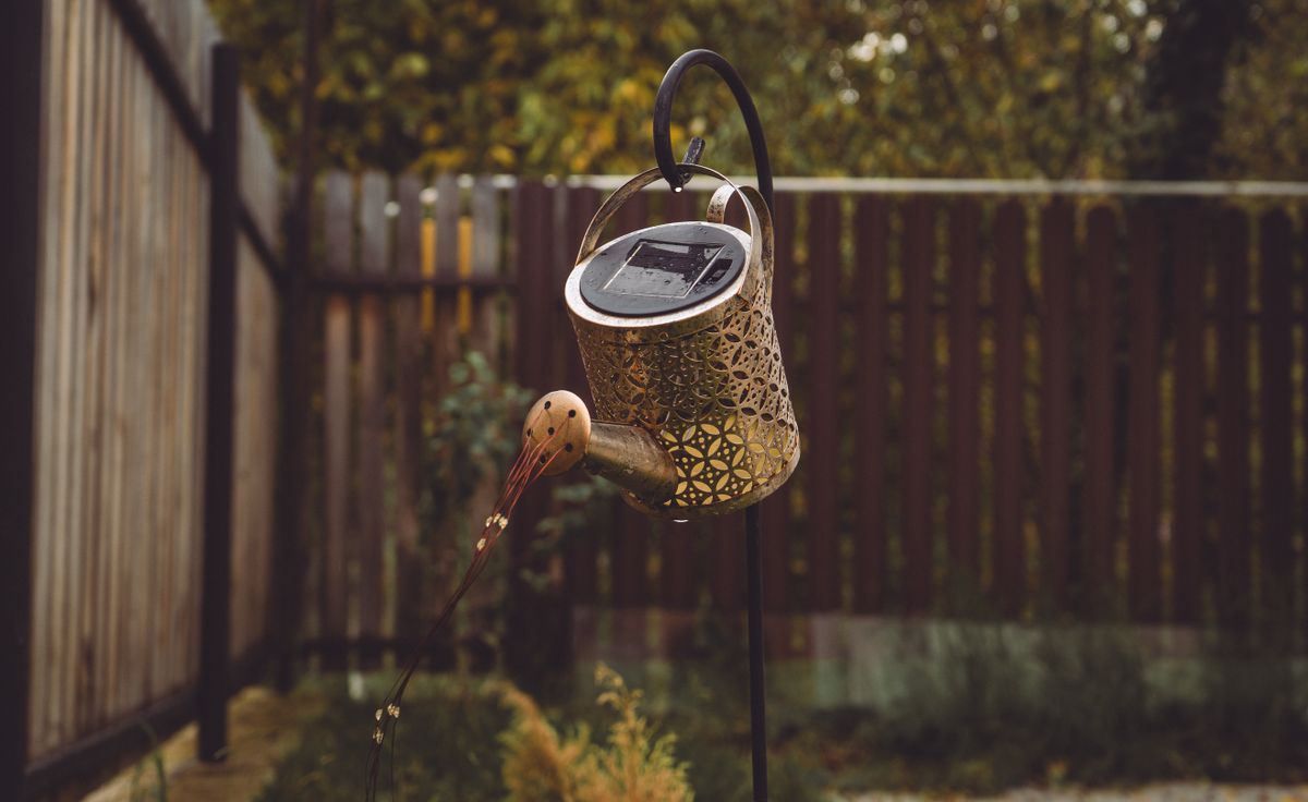 Ornate solar-powered watering can lantern adds charm to a cozy backyard garden setting.
