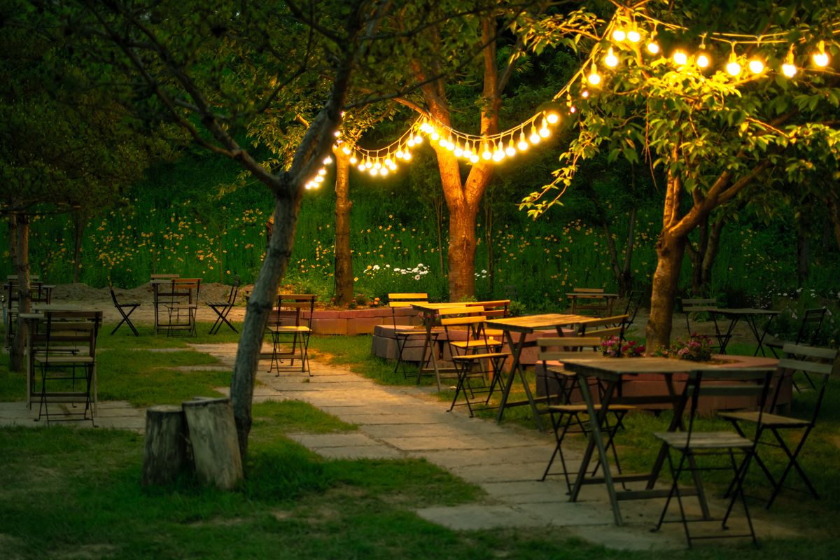 Cozy outdoor restaurant with wooden tables and charming string lights in a garden setting.
