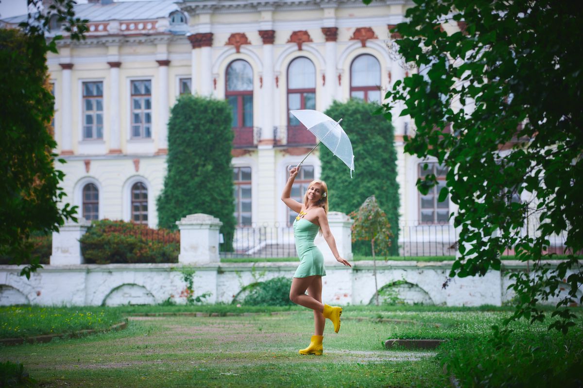 Woman in a mint dress and yellow boots enjoying a walk with an umbrella in a lush garden.