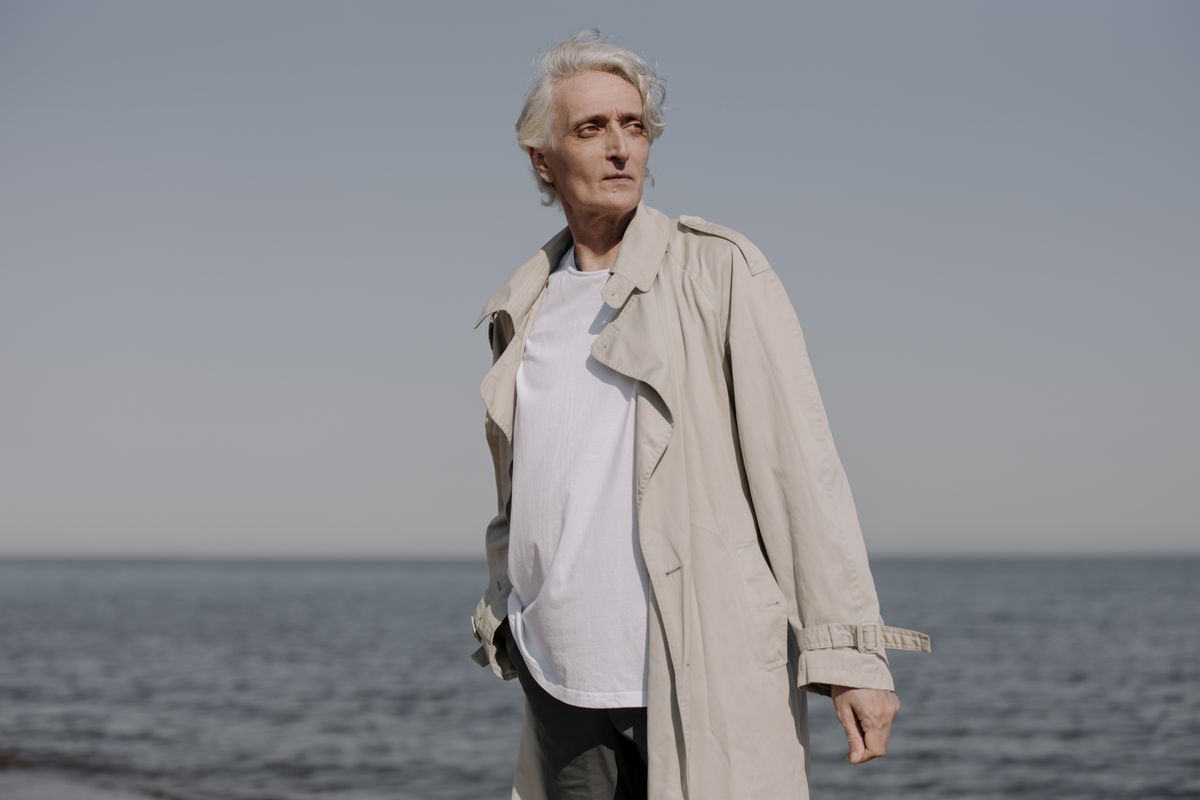 Fashionable elderly man with white hair in a trench coat standing by the sea.