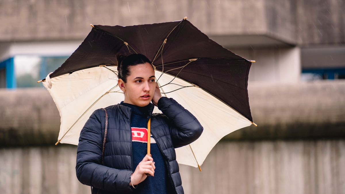 Woman holding an umbrella in an urban setting, showcasing modern fashion.