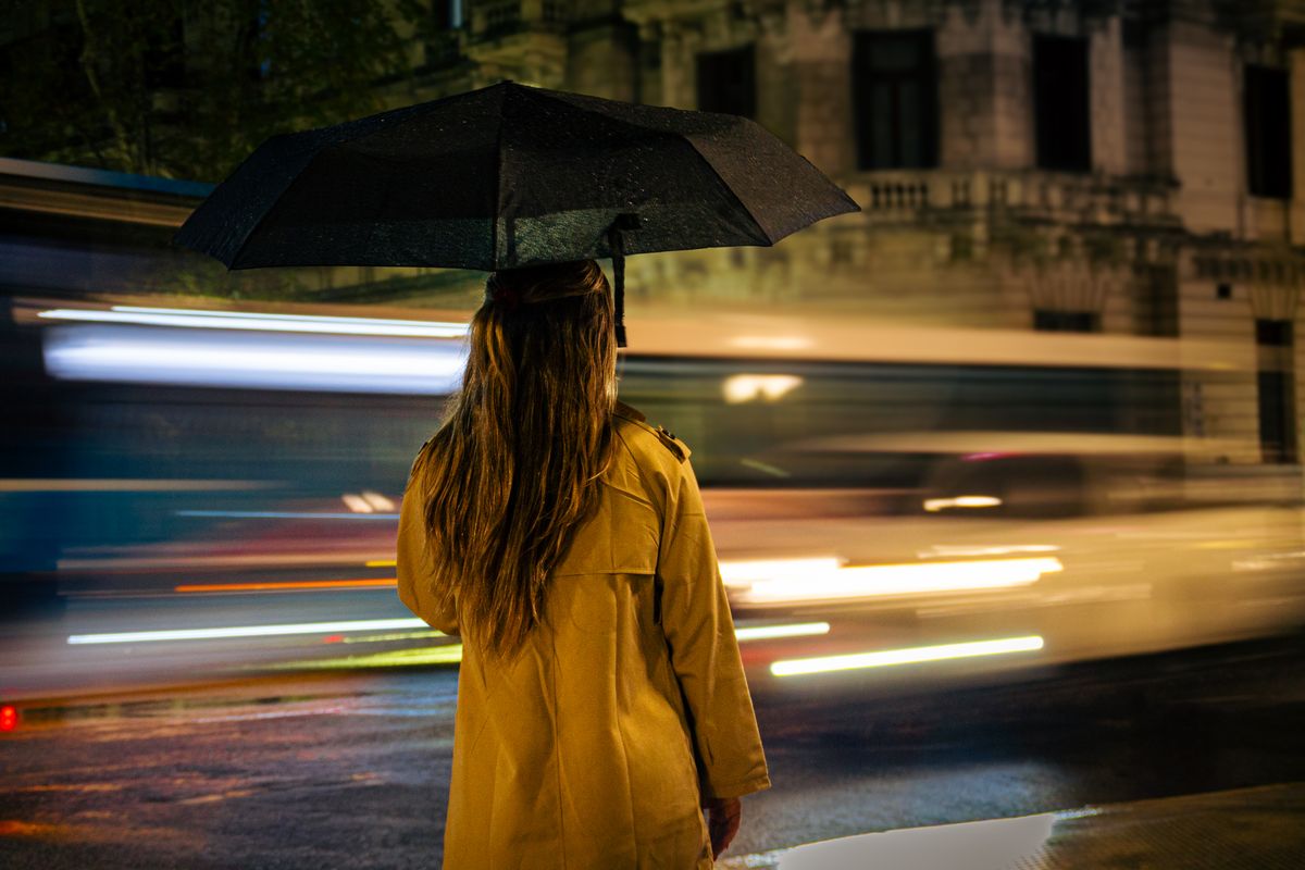 Woman with umbrella standing on a rainy night as blurred traffic passes by in Buenos Aires.