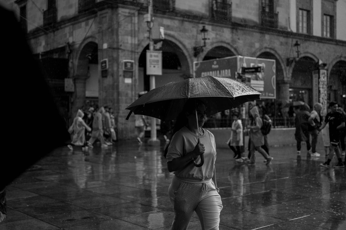 A woman walks under an umbrella during rain in a busy city street.