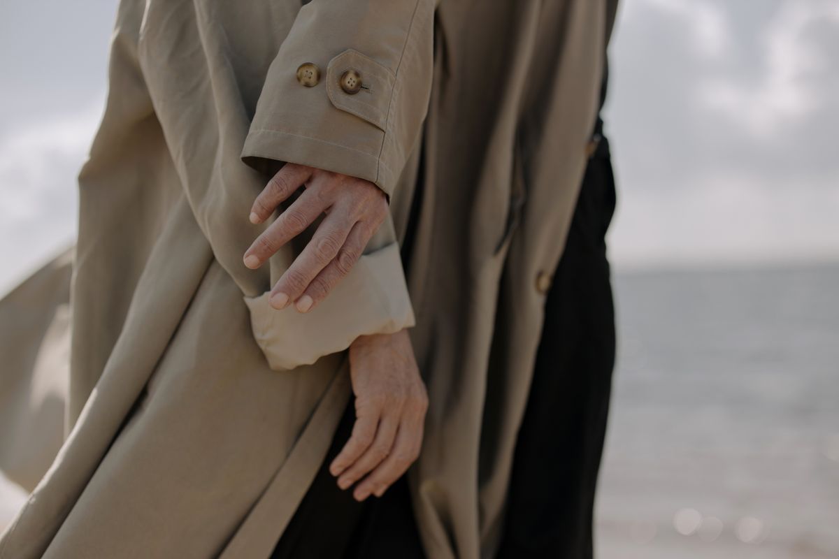 Elegant close-up of a person in a coat at the seashore showcasing fashion style.