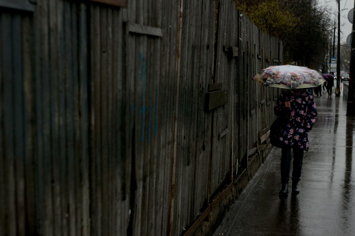 A person wearing a floral jacket walks with an umbrella on a rainy street, showcasing weather resilience and urban life.