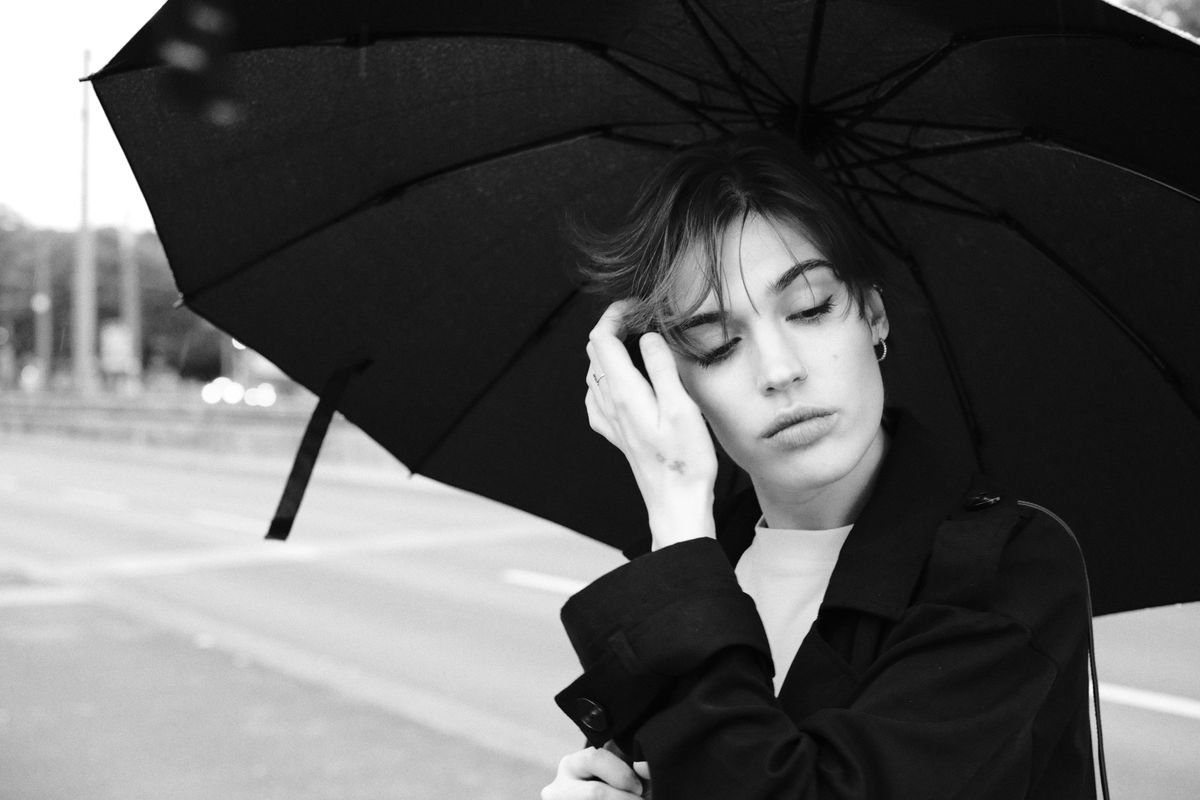 Moody black and white portrait of a woman with an umbrella on a rainy day.