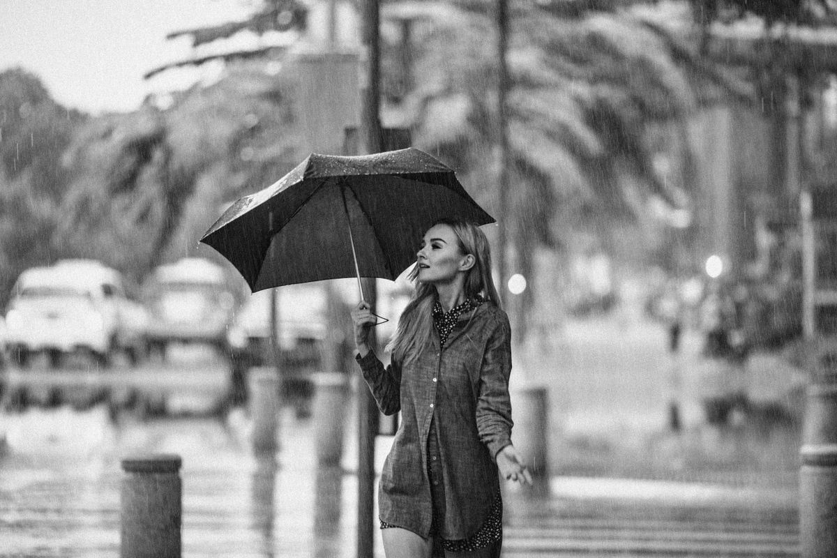 A stylish woman walking in a rainy urban street, holding an umbrella.