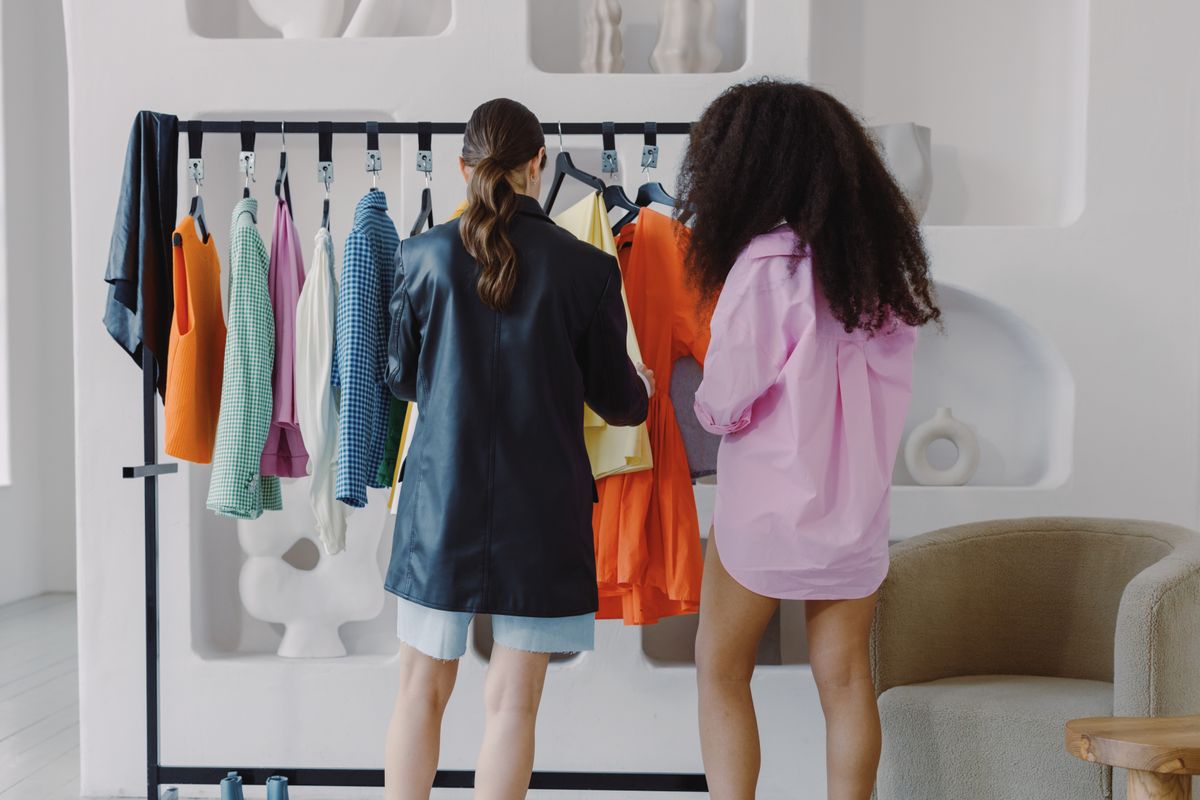 Two women selecting vibrant clothes on a rack indoors, showcasing fashion choices.