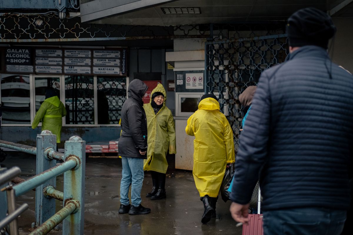 Group of people wearing raincoats walking outside a street market shop on a rainy day.